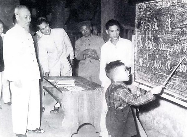 Bác Hồ đang theo dõi một cháu nhỏ đánh vần khi đến thăm lớp vỡ lòng ở phố Hàng Than, Hà Nội, năm 1958.